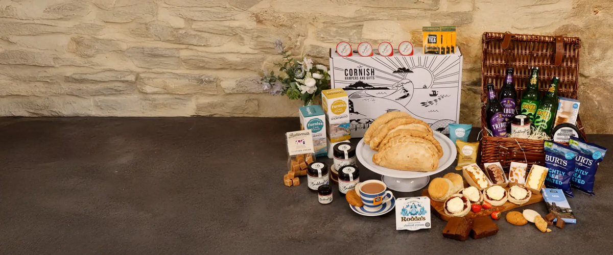 Cornish Hampers & Gifts hamper spread with pasties, cream tea and ales against a stone wall